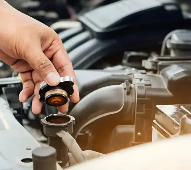 Hand removing radiator cap. This image might be relevant when researching radiator hose replacement cost.