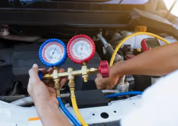 A mechanic uses a manifold gauge set to check for a freon leak in a car's AC system.