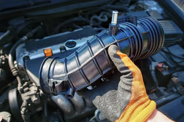 Hand in glove holds a new p0172 chevy air intake hose, ready to be installed on the engine.