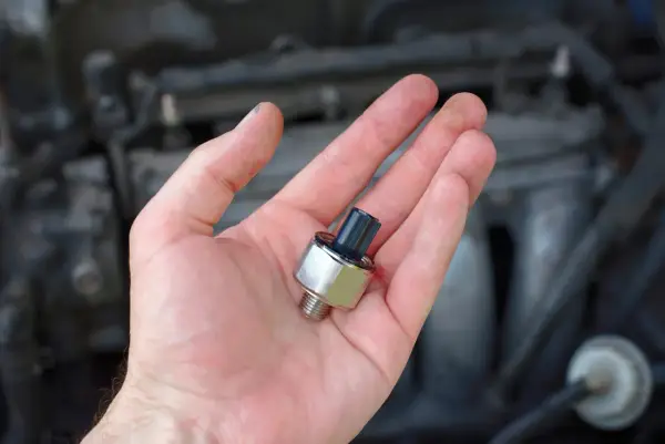 A hand holds a new oil pressure sensor, a potential fix for a p0332 code Chevy Silverado.