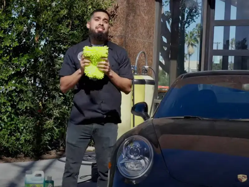 Man holding a fluffy wash mitt, ready to demonstrate how to wash a convertible car.